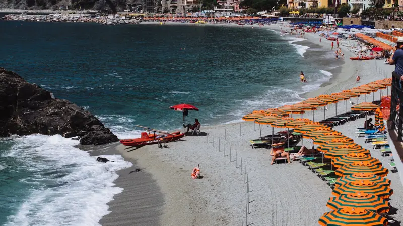 Mediteranska plaža sa suncobranima, ležaljkama i stjenovitim rtom